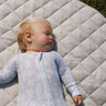 Baby lying on a soft, quilted linen play mat in pastel colors, surrounded by cozy, safe space for play.