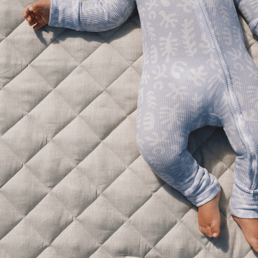 Baby lying on a soft, quilted linen play mat in pastel colors, surrounded by cozy, safe space for play.